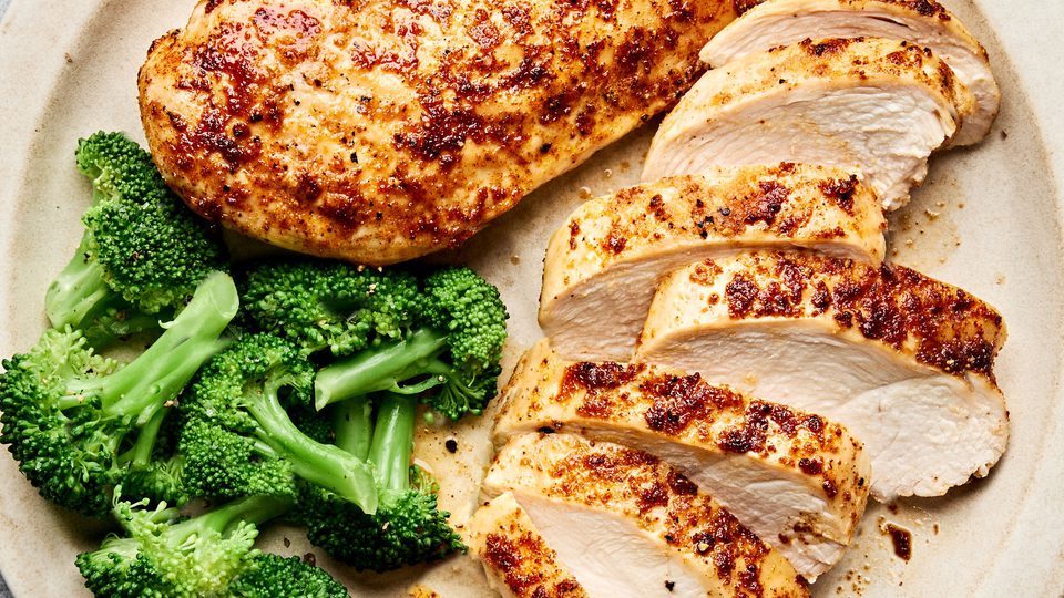 Air fryer chicken breasts cooked until golden sliced on a plate served with steamed broccoli