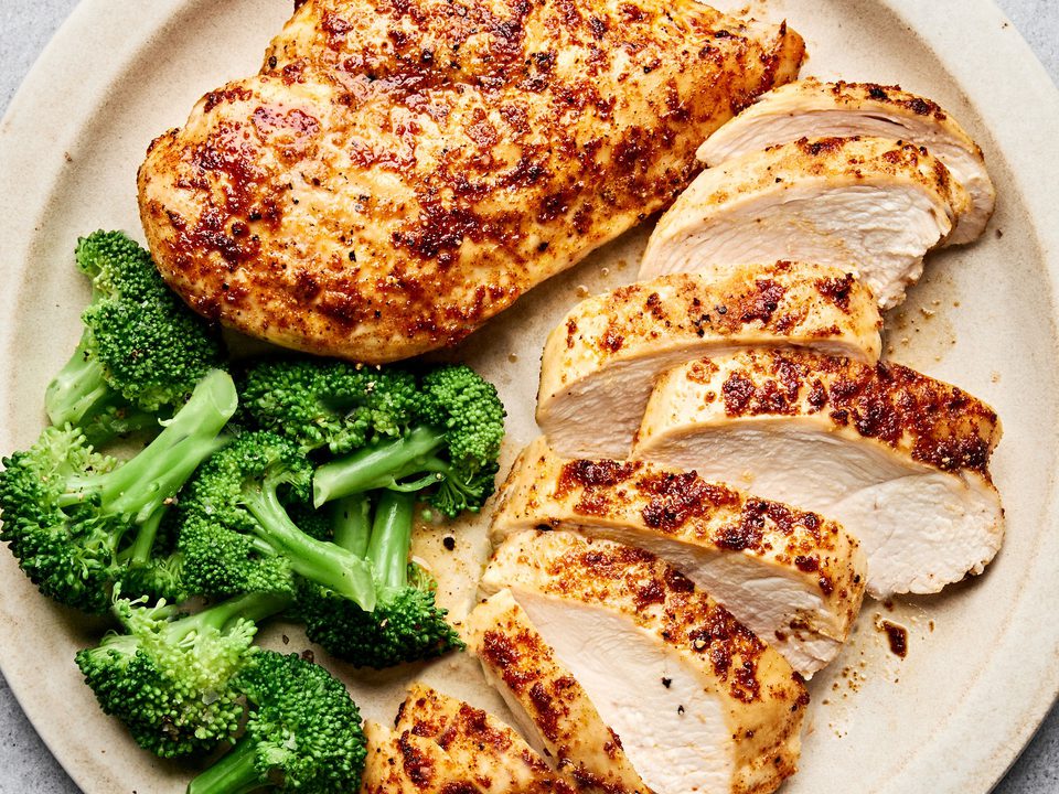 Air fryer chicken breasts cooked until golden sliced on a plate served with steamed broccoli