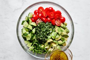avocado salad made with tomatoes, cucumbers, serrano pepper and fresh herbs being drizzled with vinaigrette