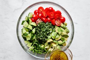 avocado salad made with tomatoes, cucumbers, serrano pepper and fresh herbs being drizzled with vinaigrette
