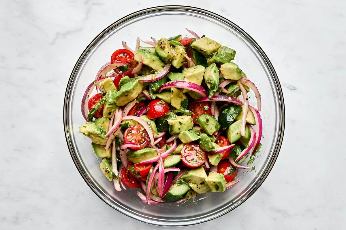 a bowl of avocado salad made with tomatoes, cucumbers, serrano pepper, cilantro, mint and homemade vinaigrette