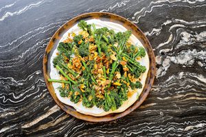 a plate of crispy air fried baby broccoli on top of whipped cottage cheese sprinkled with lemon garlic crisp and fresh dill