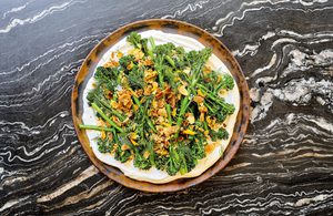 a plate of crispy air fried baby broccoli on top of whipped cottage cheese sprinkled with lemon garlic crisp and fresh dill