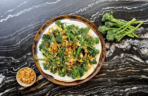 a plate of crispy air fried baby broccoli on top of whipped cottage cheese sprinkled with lemon garlic crisp and fresh dill