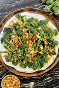 a plate of crispy air fried baby broccoli on top of whipped cottage cheese sprinkled with lemon garlic crisp and fresh dill