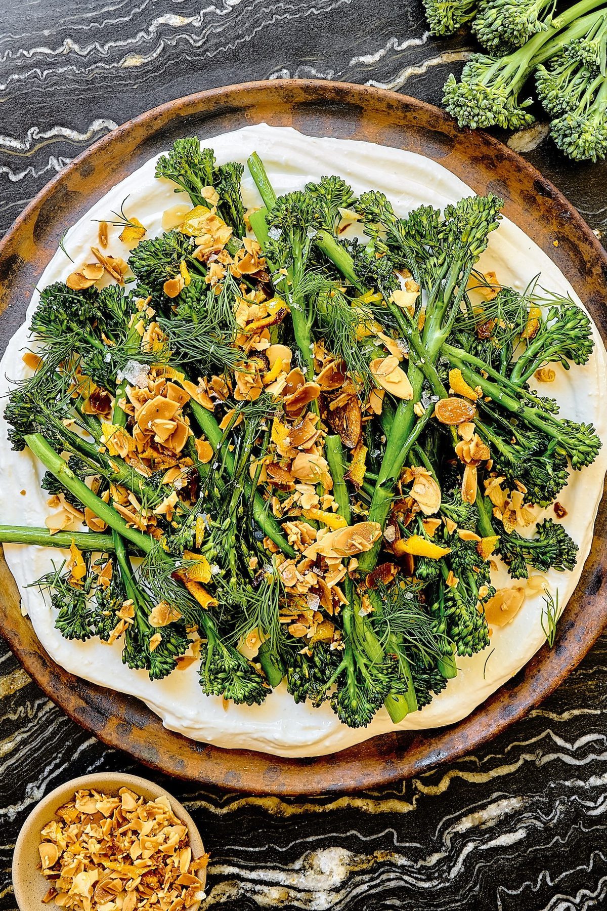a plate of crispy air fried baby broccoli on top of whipped cottage cheese sprinkled with lemon garlic crisp and fresh dill