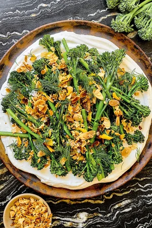 a plate of crispy air fried baby broccoli on top of whipped cottage cheese sprinkled with lemon garlic crisp and fresh dill