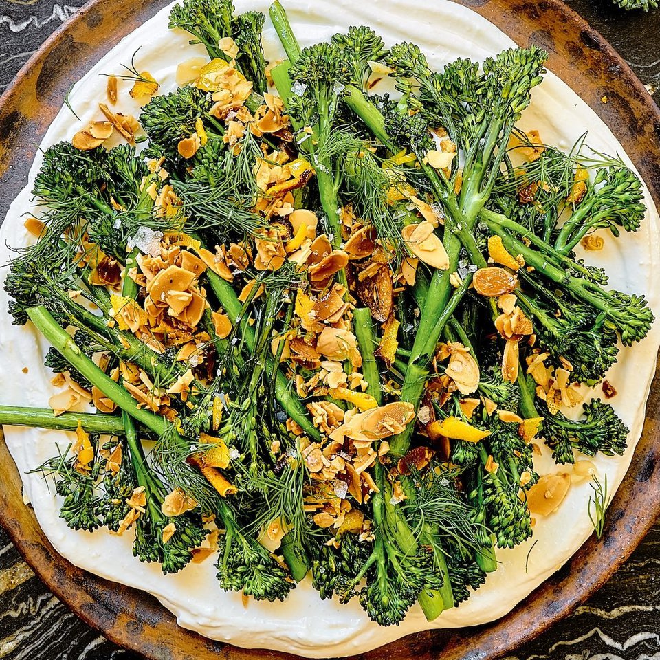 a plate of crispy air fried baby broccoli on top of whipped cottage cheese sprinkled with lemon garlic crisp and fresh dill
