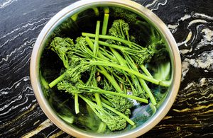 baby broccoli being tossed with olive oil, lemon juice and salt ready to be cooked in the air fyer
