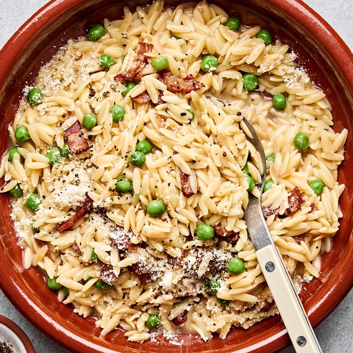 A bowl of creamy orzo pasta with peas and crispy bacon  and topped with finely grated Parmesan