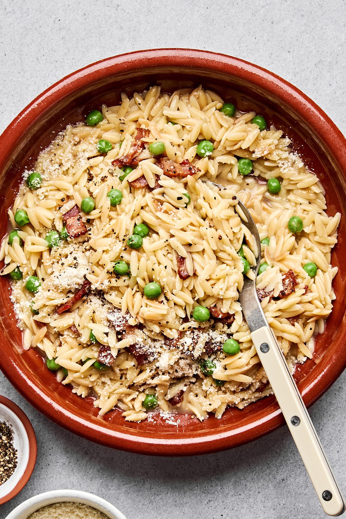 A bowl of creamy orzo pasta with peas and crispy bacon  and topped with finely grated Parmesan