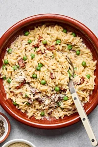 A bowl of creamy orzo pasta with peas and crispy bacon  and topped with finely grated Parmesan