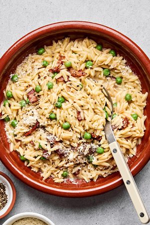 A bowl of creamy orzo pasta with peas and crispy bacon and topped with finely grated Parmesan