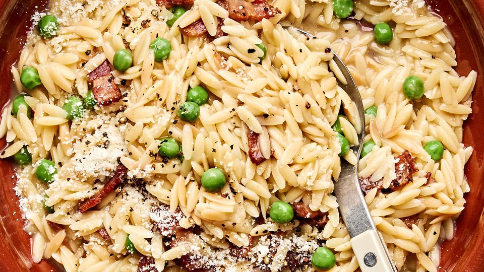 A bowl of creamy orzo pasta with peas and crispy bacon  and topped with finely grated Parmesan