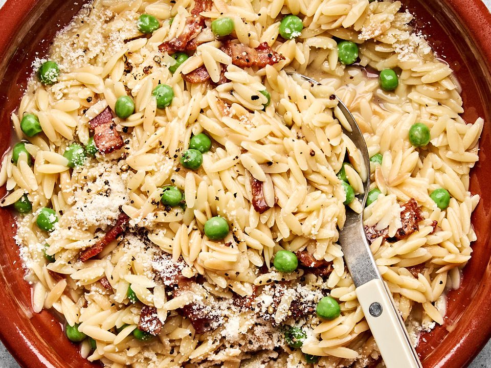 A bowl of creamy orzo pasta with peas and crispy bacon  and topped with finely grated Parmesan