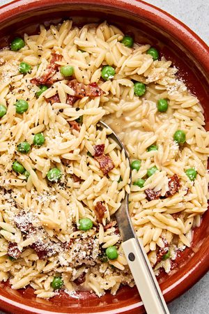 A bowl of creamy orzo pasta with peas and crispy bacon and topped with finely grated Parmesan