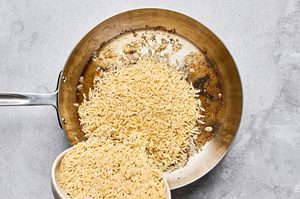 orzo pasta being poured into a pan with reserved bacon fat to make a creamy orzo with bacon and peas