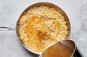 hot chicken broth being poured into a pan with bacon fat and orzo pasta to make a creamy orzo dinner
