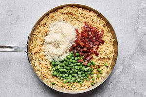 cooked orzo, parmesan, cooked chopped bacon, peas and pepper being stirred together in a pan