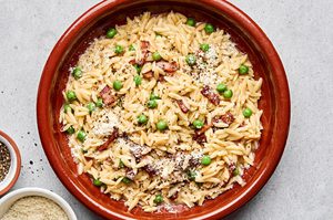 A bowl of creamy orzo pasta with peas and crispy bacon and topped with finely grated Parmesan