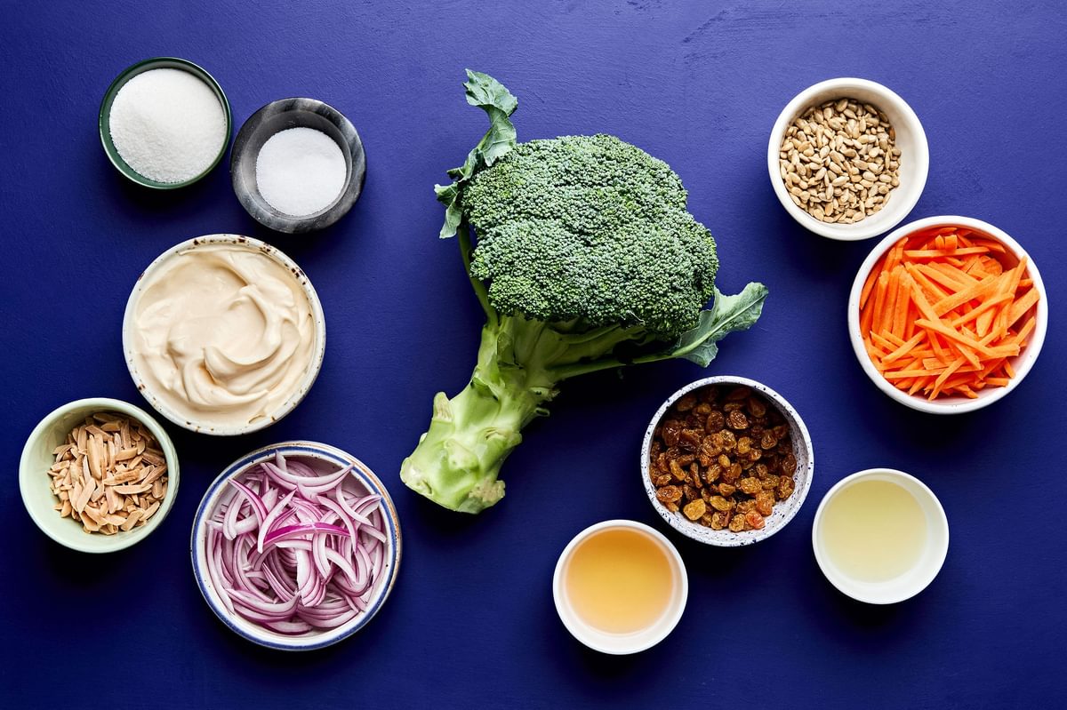 Individual bowls filled with chopped broccoli, shredded carrots and dressing ingredients for making broccoli slaw.