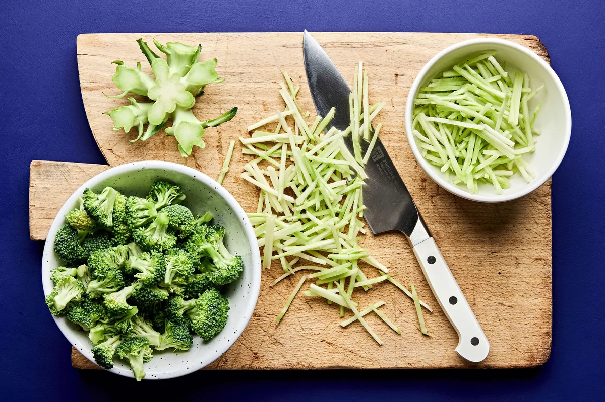 fresh broccoli being chopped and prepared on a cutting board to make homemade broccoli slaw