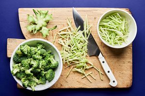 fresh broccoli being chopped and prepared on a cutting board to make homemade broccoli slaw