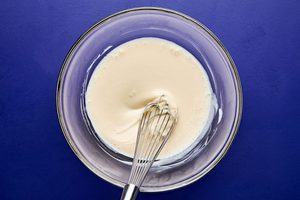Dressing for broccoli slaw in a bowl made with mayonnaise, sugar, lemon juice, vinegar, and salt whisked until smooth