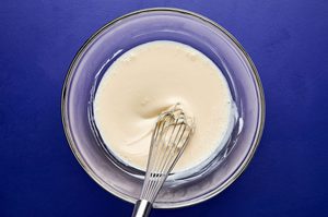 Dressing for broccoli slaw in a bowl made with mayonnaise, sugar, lemon juice, vinegar, and salt whisked until smooth