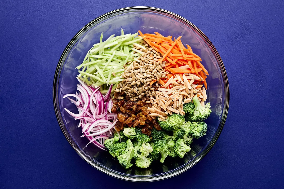 broccoli, red onion, carrots, raisins, almonds, and sunflower seeds in a bowl to make homemade broccoli slaw