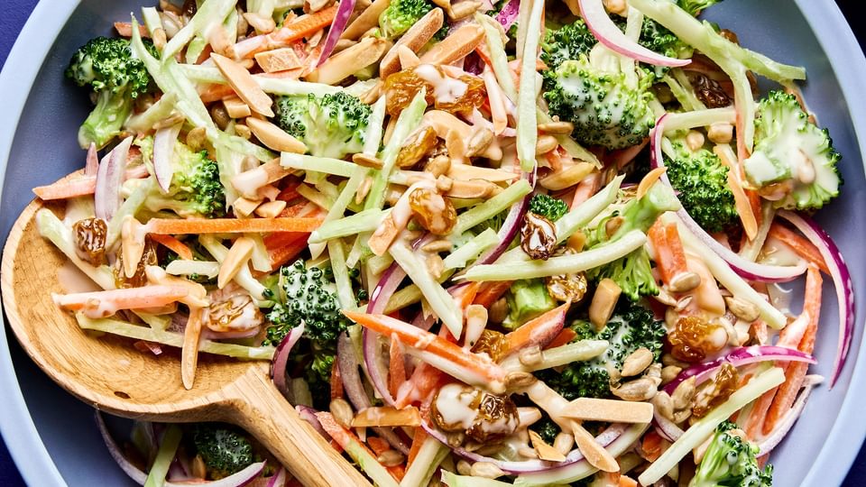 A bowl of fresh broccoli slaw with shredded carrots and cranberries and almonds, tossed in a light dressing.