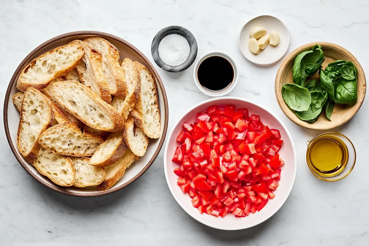 diced fresh tomatoes, sliced baguette, olive oil, fresh basil, garlic, salt and balsamic vinegar laid out to make bruschetta