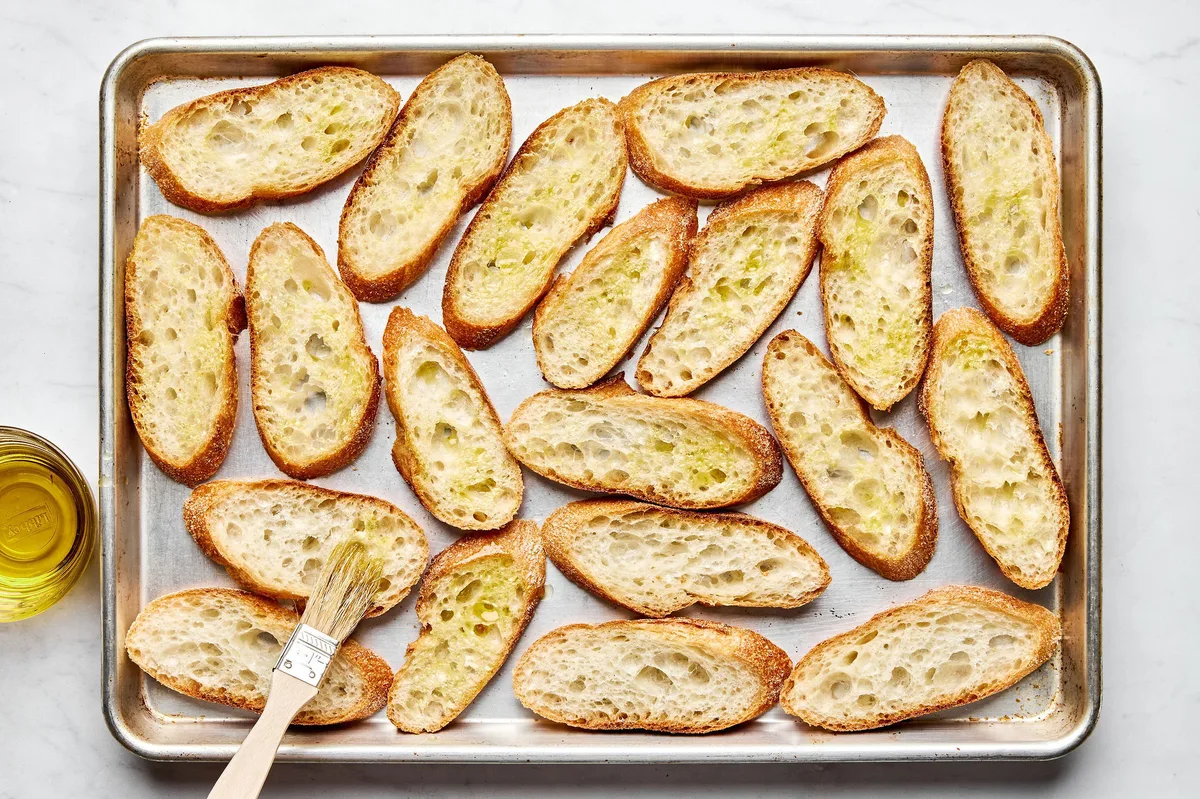 sliced baguette being brushed with olive oil on a baking sheet to make easy homemade bruschetta