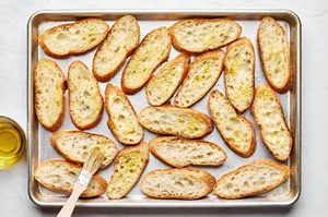 sliced baguette being brushed with olive oil on a baking sheet to make easy homemade bruschetta