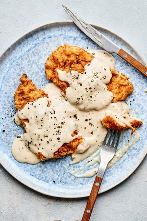 homemade Crispy chicken fried chicken topped with creamy country gravy on a plate, a classic Southern comfort food dinner