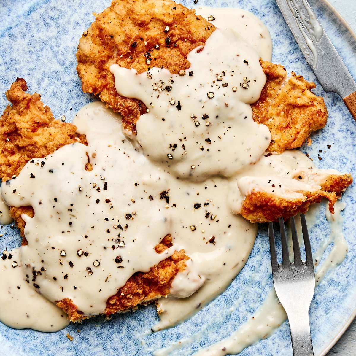 Crispy chicken fried chicken topped with creamy country gravy on a plate, a classic Southern comfort food dinner