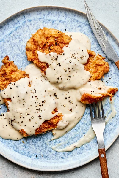 Crispy chicken fried chicken topped with creamy country gravy on a plate, a classic Southern comfort food dinner
