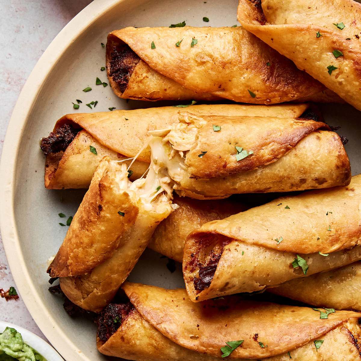 A plate of golden, crispy homemade chicken flautas served with sour cream and guacamole on the side.