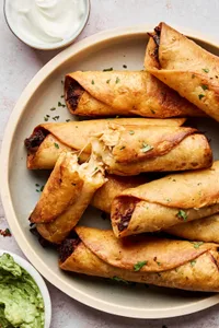 A plate of golden, crispy homemade chicken flautas served with sour cream and guacamole on the side.