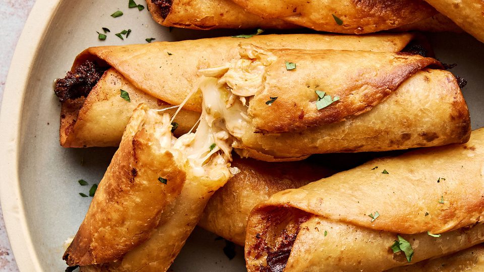 A plate of golden, crispy homemade chicken flautas served with sour cream and guacamole on the side.