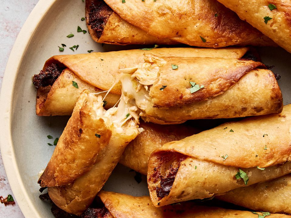 A plate of golden, crispy homemade chicken flautas served with sour cream and guacamole on the side.