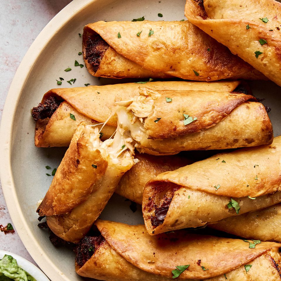 A plate of golden, crispy homemade chicken flautas served with sour cream and guacamole on the side.