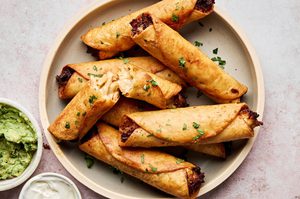 A plate of golden, crispy homemade chicken flautas served with sour cream and guacamole on the side.