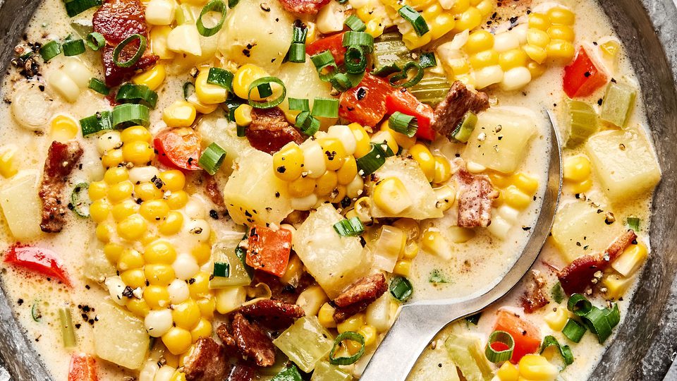 A bowl of creamy homemade corn chowder with potatoes, bell pepper and crispy chopped bacon and topped with green onion