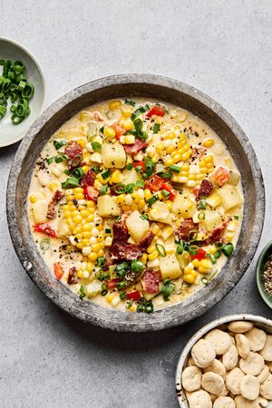 A bowl of creamy homemade corn chowder with potatoes, bell pepper and crispy chopped bacon and topped with green onion