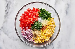 ingredients to make fresh corn salsa being tossed together in a bowl