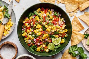 Bowl of fresh corn salsa with diced tomatoes, red onion, jalapeño, cilantro, and lime served with crispy tortilla chips