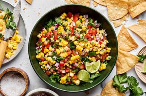 Bowl of fresh corn salsa with diced tomatoes, red onion, jalapeño, cilantro, and lime served with crispy tortilla chips