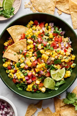 Bowl of fresh corn salsa with diced tomatoes, red onion, jalapeño, cilantro, and lime served with crispy tortilla chips