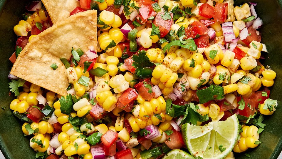 Bowl of fresh corn salsa with diced tomatoes, red onion, jalapeño, cilantro, and lime surrounded by crispy tortilla chips